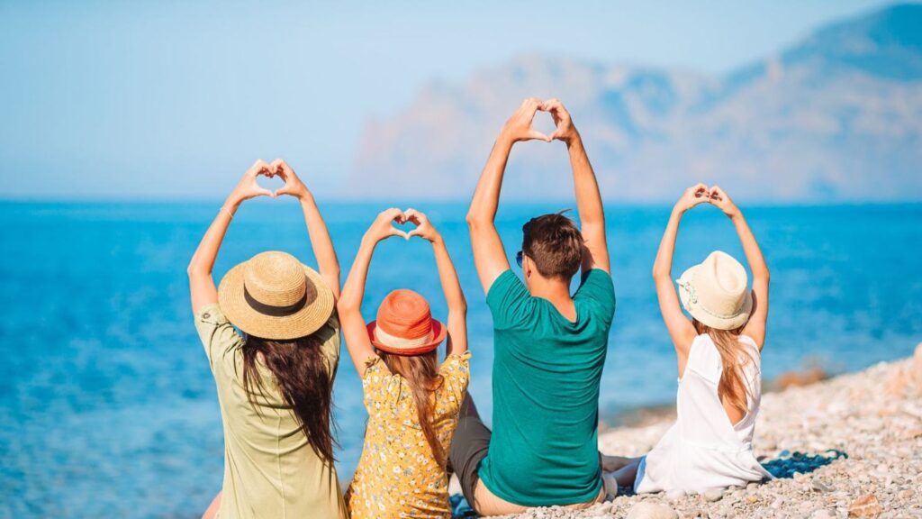 A happy family sitting on a beach in Cairns, making heart shapes with their hands by the ocean