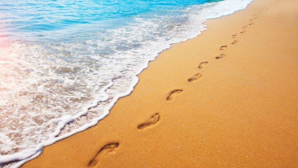 Footprints on golden sand with gentle ocean waves at a tropical beach in Cairns